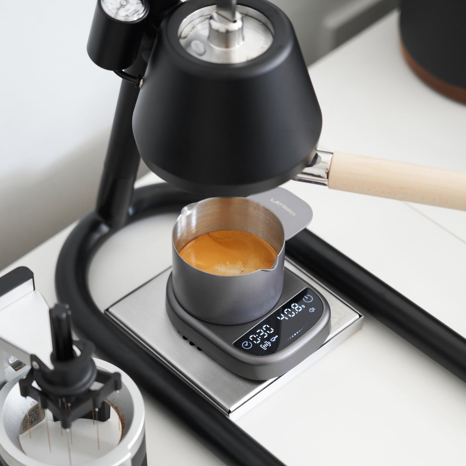 Compact coffee scale timing an espresso shot below an espresso machine