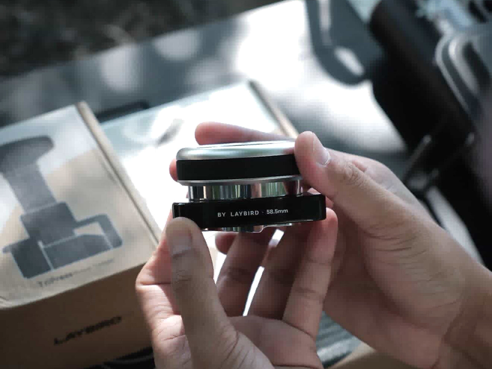 Hands holding the 58.5mm LAYBIRD TriSpin adjustable-depth coffee distributor
